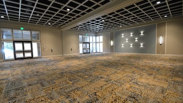 A spacious room with a patterned carpet, a grid ceiling, and large windows with blinds.