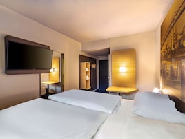 Habitación de hotel con dos camas, un televisor de pantalla plana en la pared y un cuadro de una escena industrial.