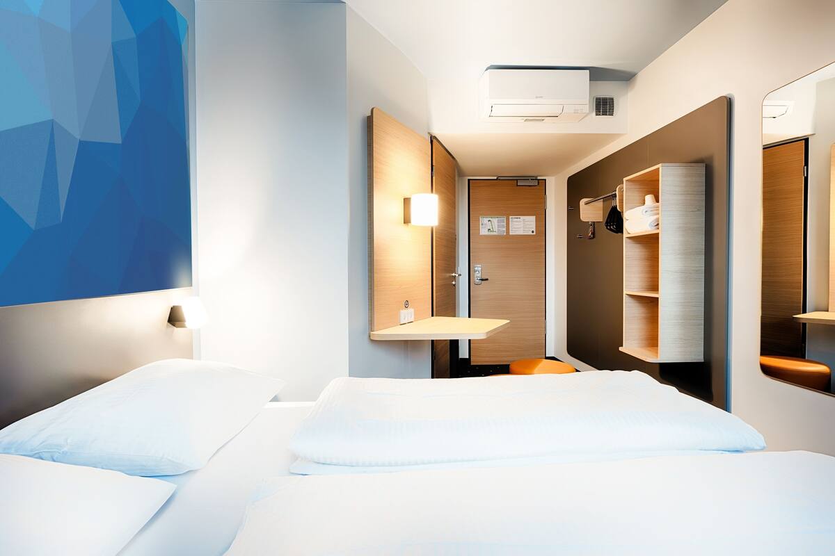 Een hotelkamer met twee bedden, een badkamer met spiegel en een wandairconditioner.