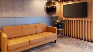 A modern living room with a sofa, a round mirror, a flat-screen TV, and a decorative vase.
