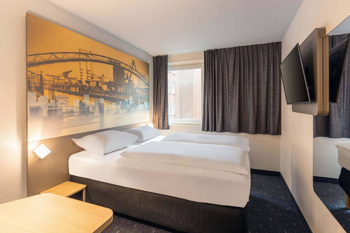 Een hotelkamer met een groot bed, een bureau, een flatscreen televisie aan de muur en een raam met gordijnen.