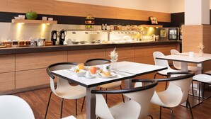 Een moderne eetruimte met witte tafels en stoelen, een buffet met diverse gerechten en een koelkast op de achtergrond.