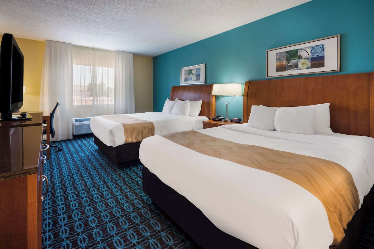 A hotel room with two beds, a TV, a desk, and a window with curtains.
