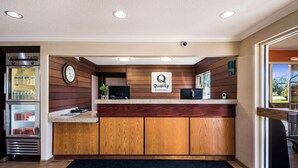 A hotel reception area with wooden paneling, a clock, a refrigerator stocked with bottled water, and a sign indicating 'Quality by Choice Hotels'. - Quality Inn & Suites Bozeman (Bozeman)