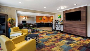 A hotel lobby with yellow seating, a patterned carpet, a kitchen area, and a flat-screen TV mounted on the wall. - Quality Inn & Suites Bozeman (Bozeman)