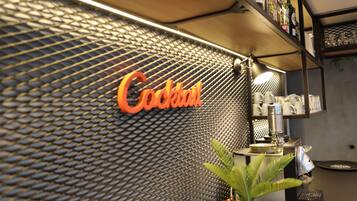 A bar area with a 'Cocktail' sign on a textured wall, a plant, and barware on shelves.