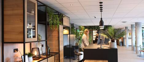Un área de recepción moderna con un mostrador de madera, vitrinas de vidrio y plantas en macetas.