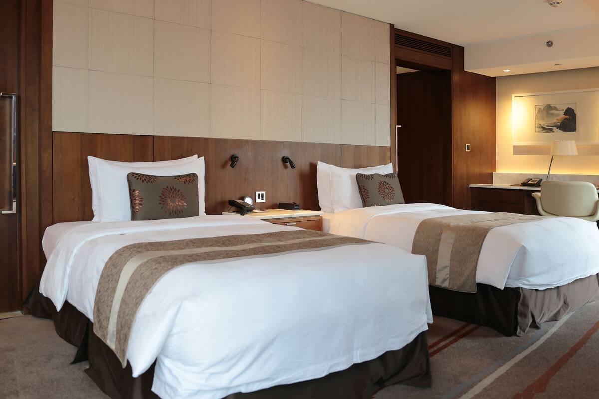 A hotel room with two beds, a desk, a chair, and a large painting on the wall.