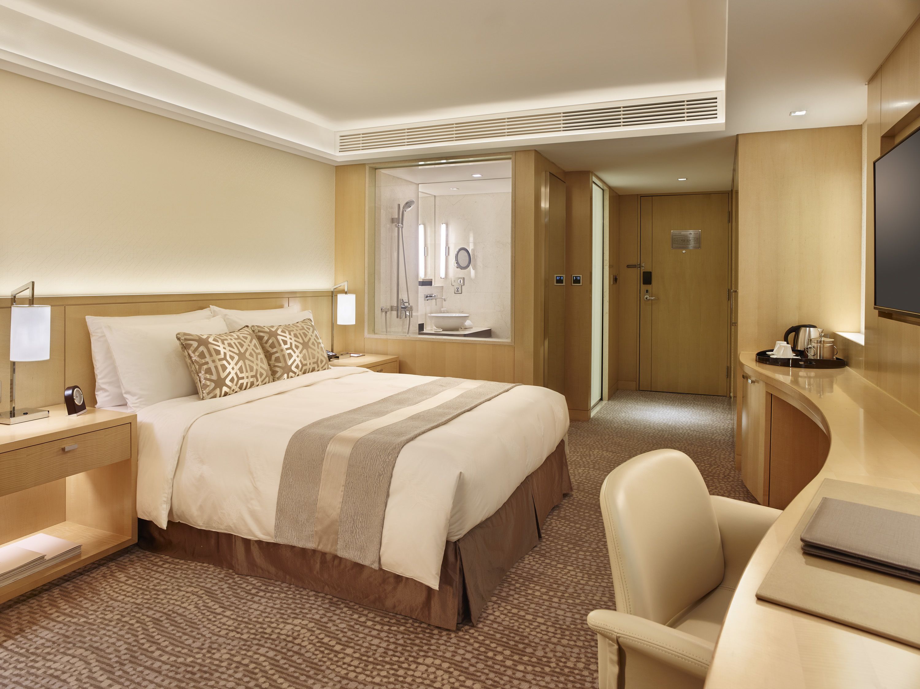 A hotel room with a large bed, a desk, a chair, a TV, and a bathroom visible through an open door.