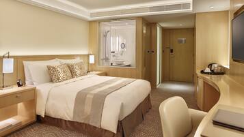 A hotel room with a large bed, a desk, a chair, a TV, and a bathroom visible through an open door.
