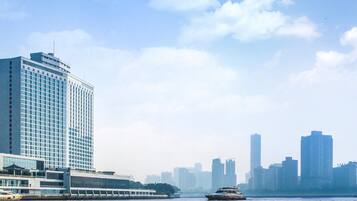 A high-rise hotel with a modern glass facade, situated by a waterfront with a view of the city skyline.