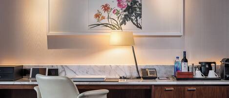 A modern hotel room with a marble countertop, a desk with a lamp, a chair, a phone, a water bottle, and a coffee maker.