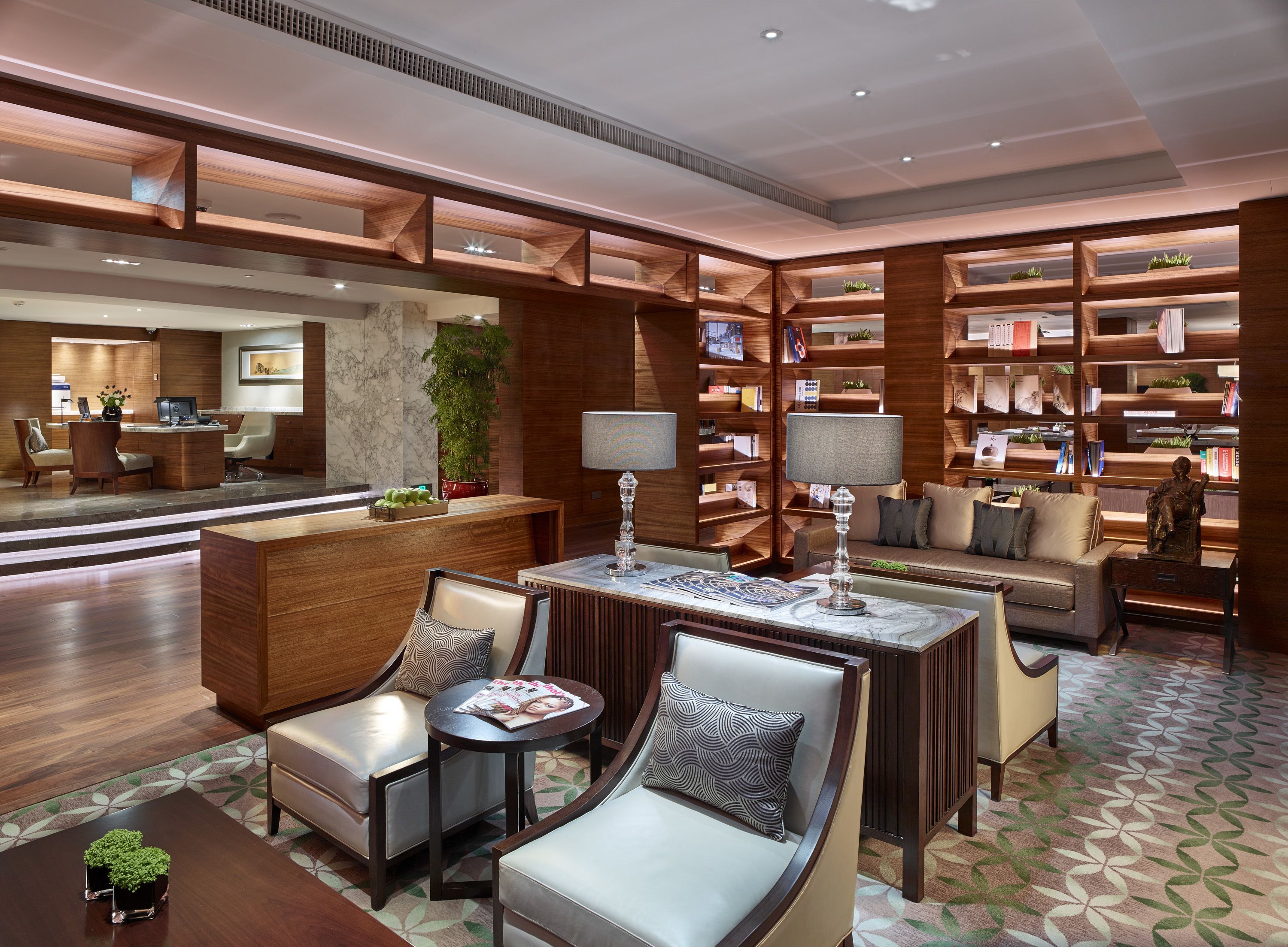 A modern lobby with a reception desk, seating area, and a bookshelf filled with books and decorative items.