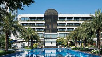 Un hotel con piscina central, rodeado de palmeras y un cielo azul despejado.