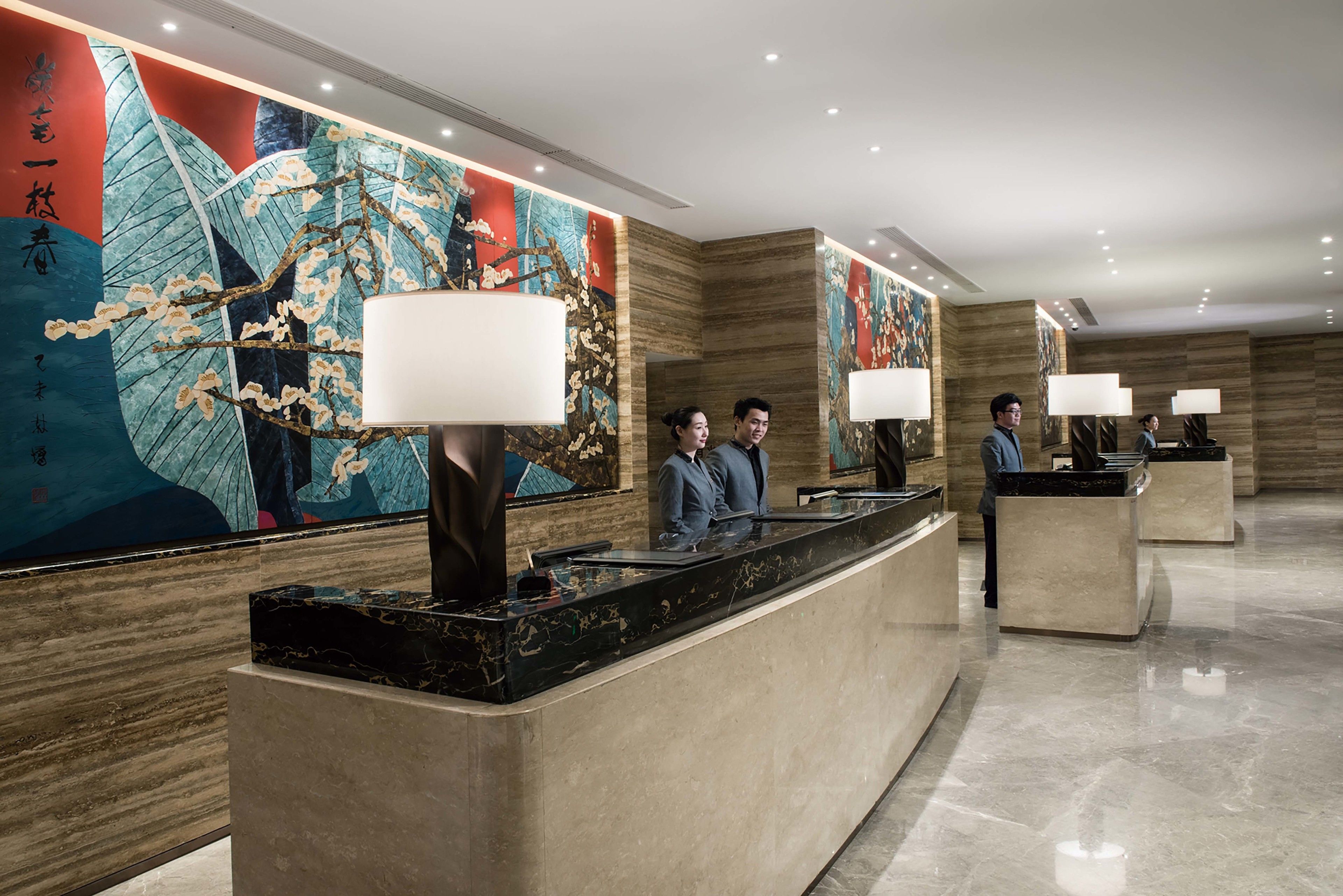 A hotel reception area with marble counters, large wall paintings, and modern lighting.
