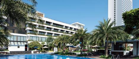 A hotel with a swimming pool, palm trees, and a tall building in the background.