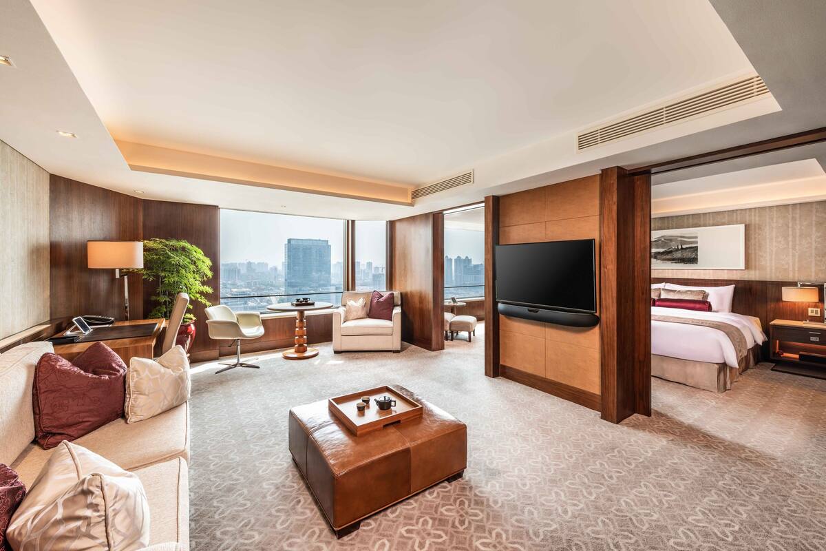 A modern hotel room with a large bed, a TV, a sofa, a coffee table, and a city view.