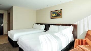 A hotel room with two beds, a large window, and a painting on the wall.