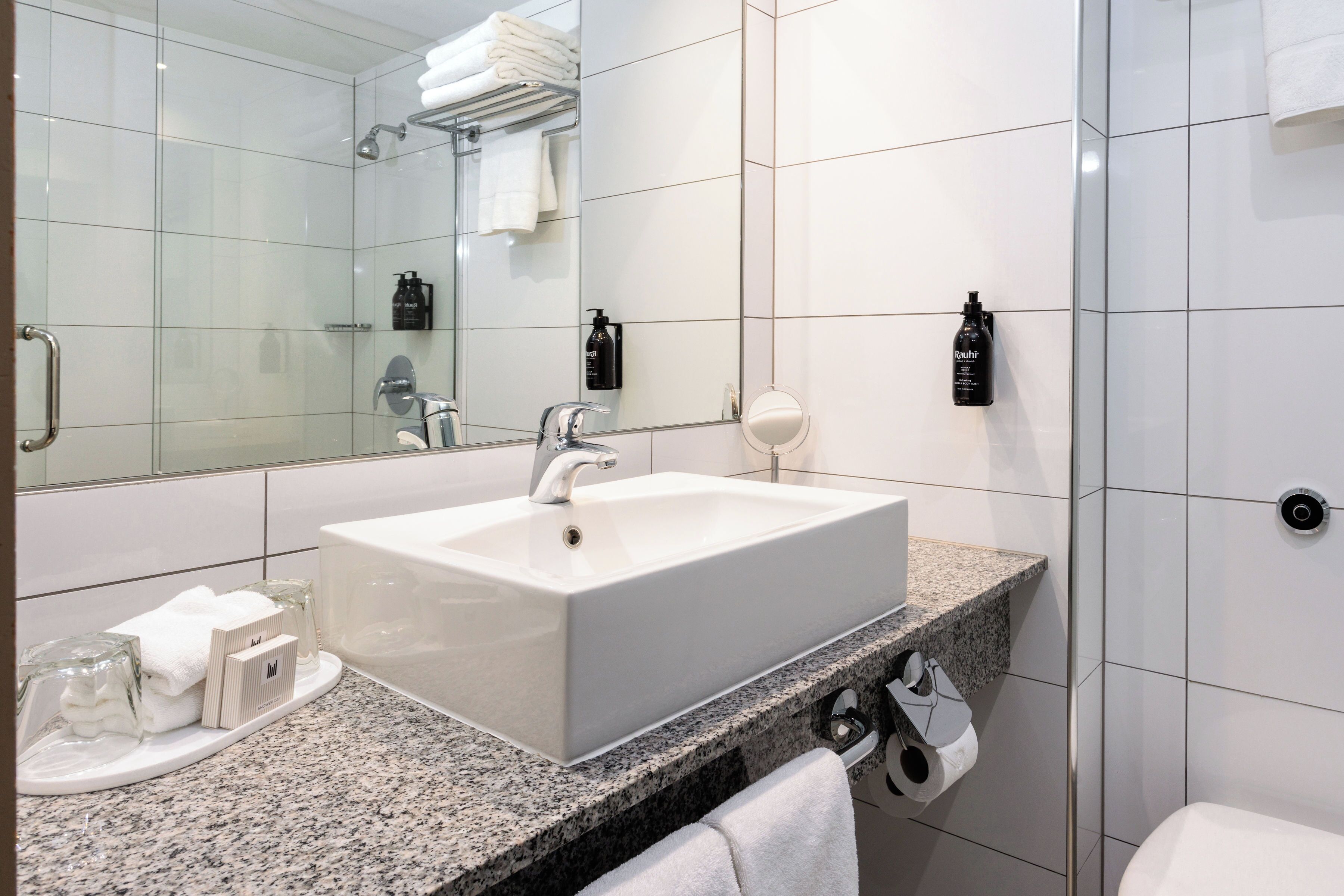 A modern bathroom with a large mirror, white sink, and granite countertop.