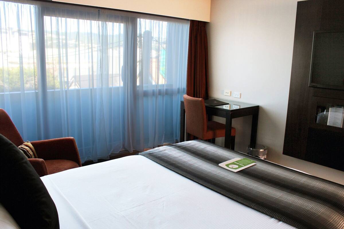 A hotel room with a bed, a desk, a chair, and a television.