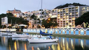 A marina with several boats docked, a large building with multiple balconies, and a hillside with residential buildings. - Copthorne Hotel Wellington Oriental Bay (Wellington)
