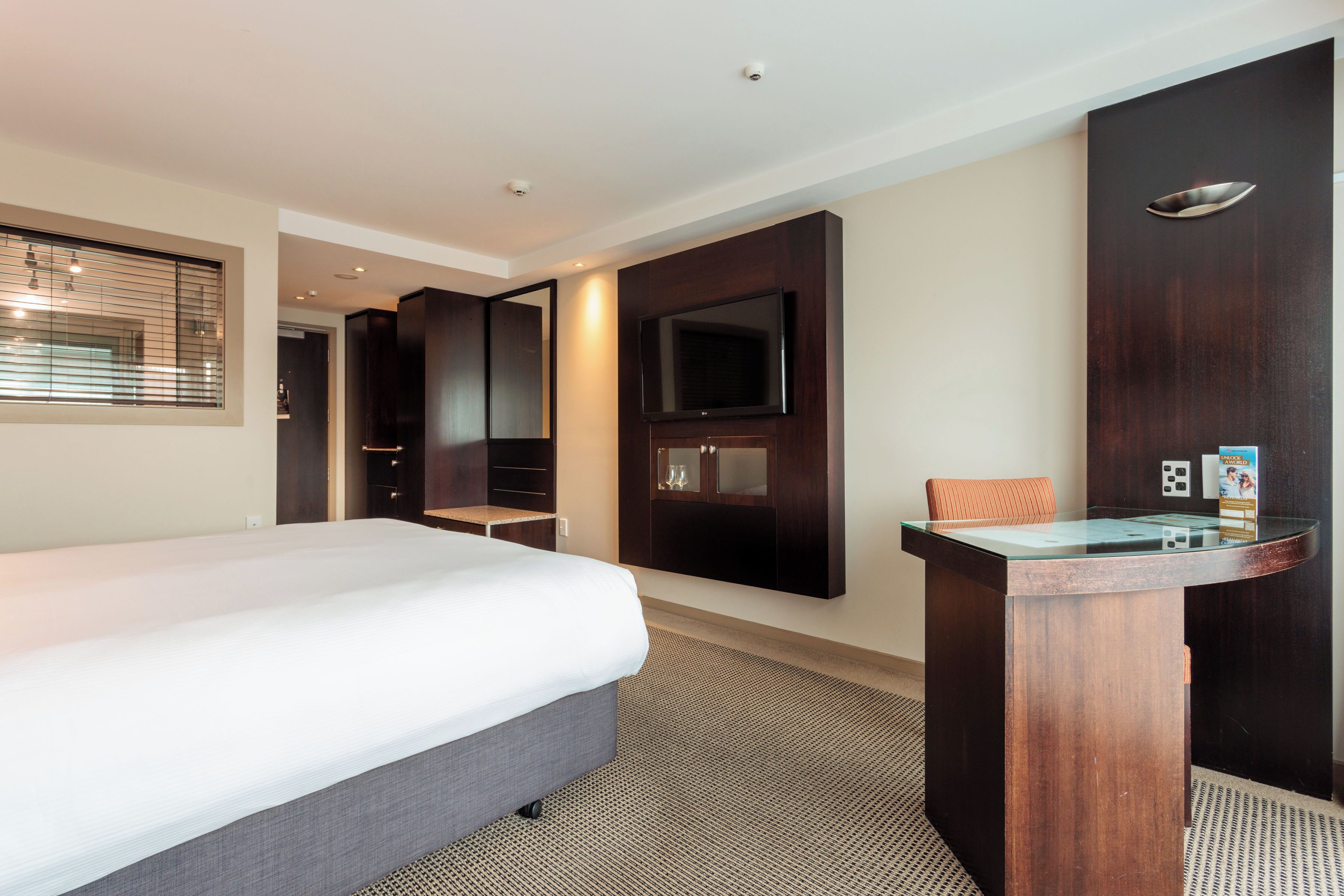Habitación de hotel con una cama grande, un televisor montado en la pared, un escritorio pequeño y un espejo.