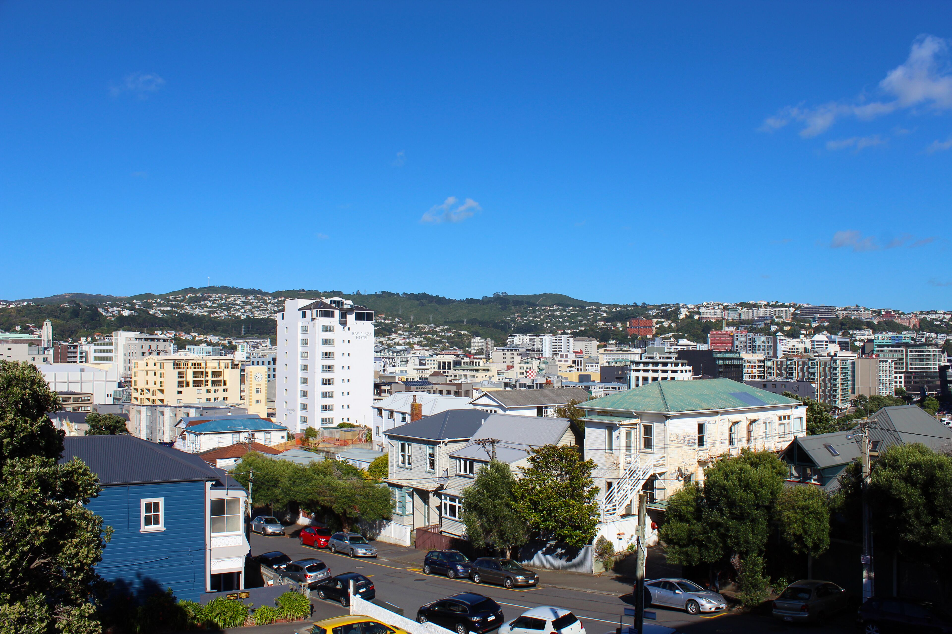 A cityscape with a mix of residential and commercial buildings, including a prominent white building with a green roof and a blue building with a dark roof.