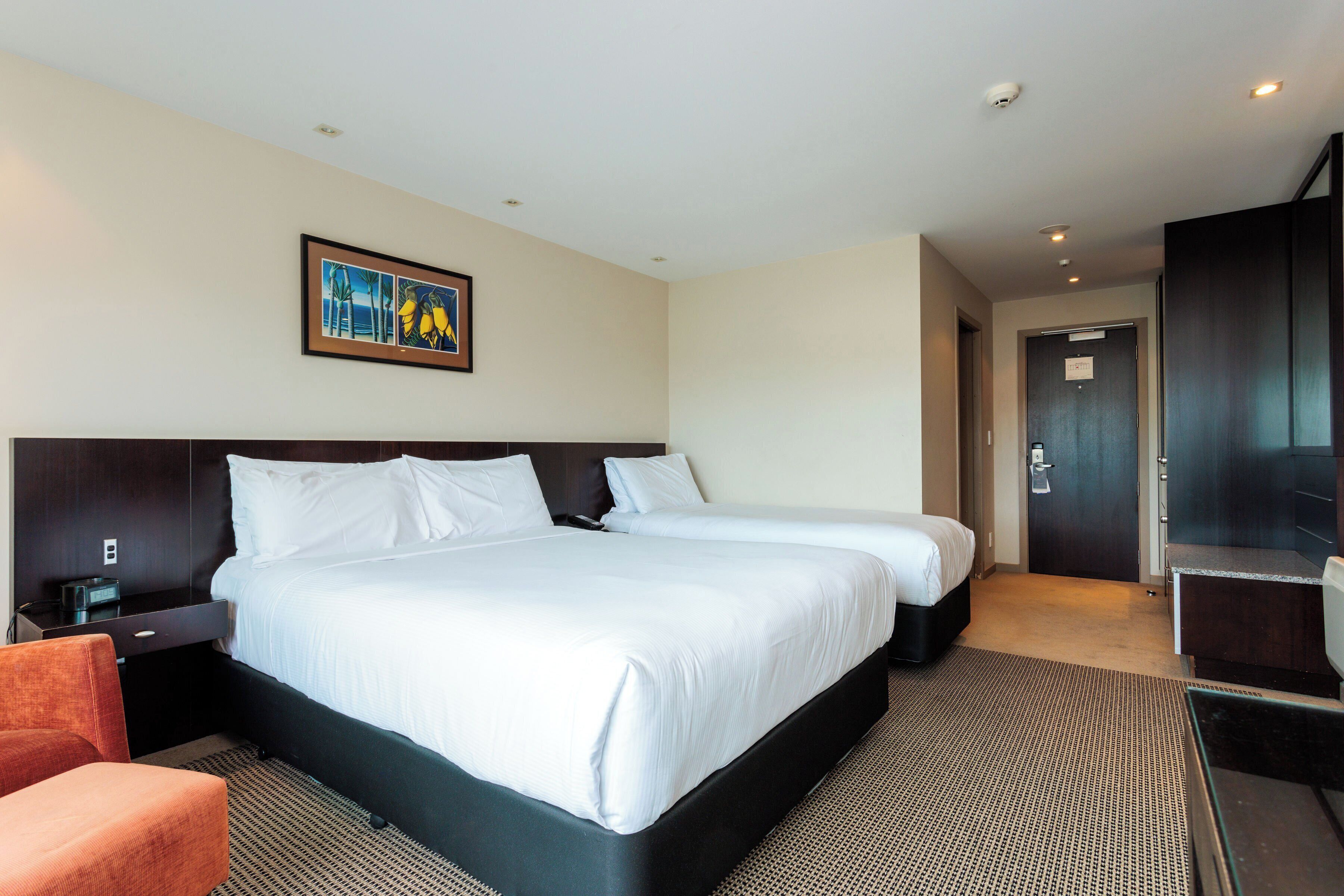 A hotel room with two beds, a desk, a chair, and a painting on the wall.