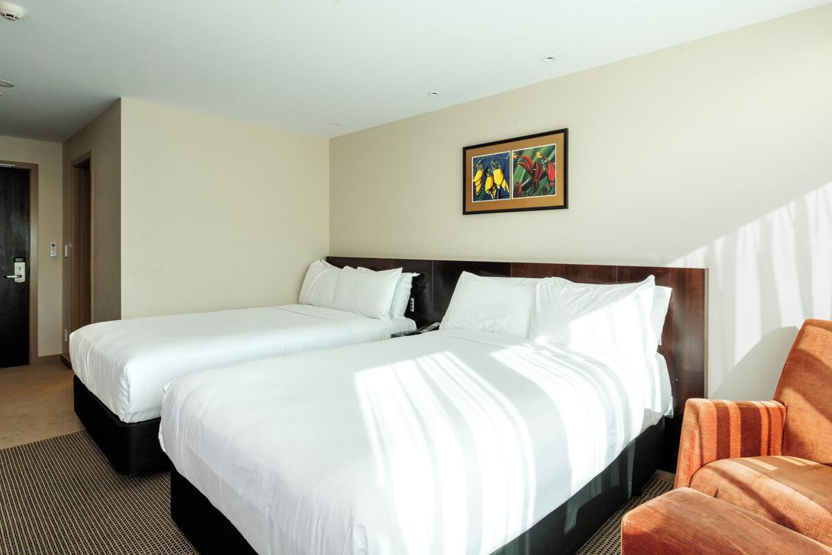 A hotel room with two beds, a wooden headboard, a framed artwork on the wall, and a striped armchair.