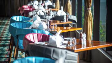 Un restaurante con varias mesas, cada una con manteles blancos, sillas azules y rosadas, y cubertería dispuesta cuidadosamente.