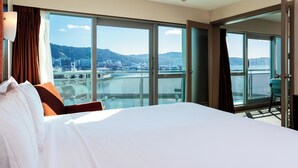 A hotel room with a large bed, a view of a cityscape and water, and a balcony with a chair. - Copthorne Hotel Wellington Oriental Bay (Wellington)