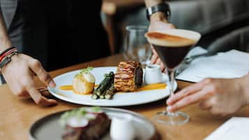 A dining table with a plate of food, a glass of drink, and a person wearing a watch.