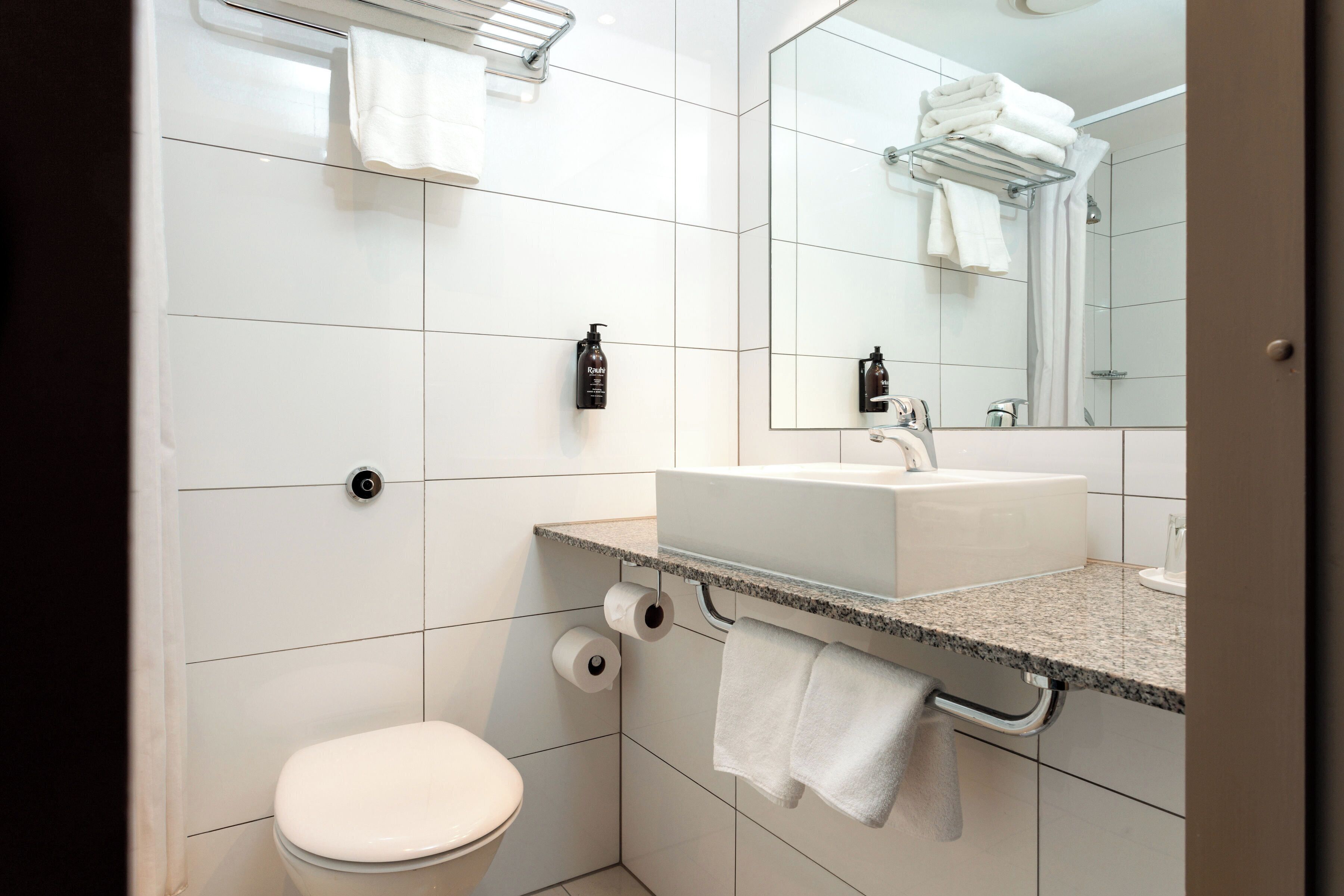Un baño moderno con inodoro blanco, lavamanos con espejo y toallero con toallas.