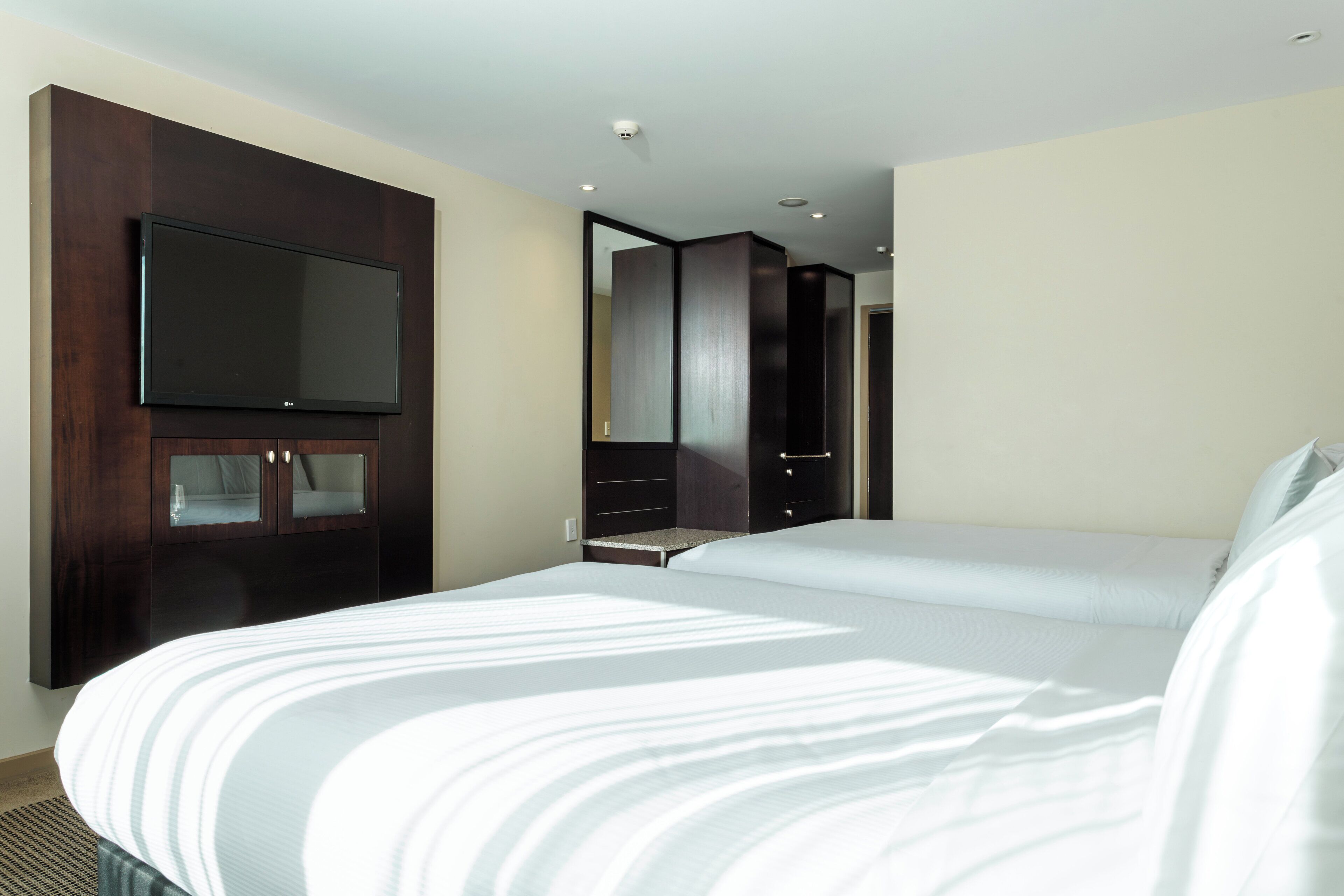Habitación de hotel con una cama grande, un televisor de pantalla plana montado en un mueble de madera y un espejo en la pared.