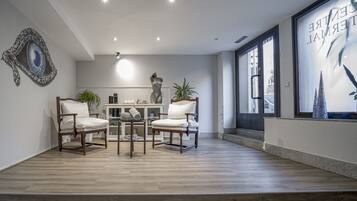 Una habitación amplia con suelo de madera, una mesa central con sillas, un ventanal con vistas y un espejo decorativo en la pared.