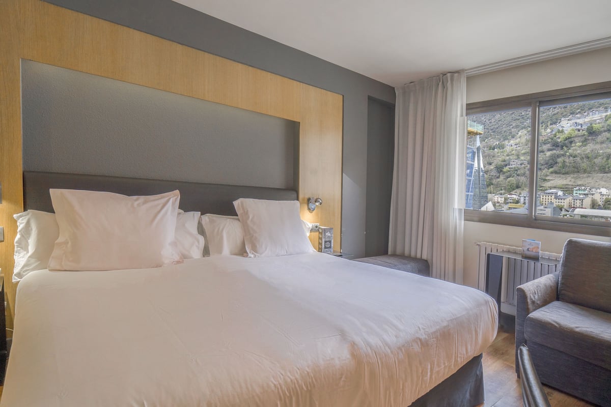 Quarto de hotel com uma cama grande, mesa de cabeceira com telefone e uma cadeira.