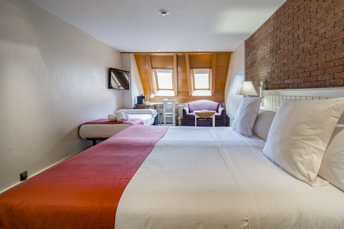 Quarto de hotel com cama, escrivaninha, cadeira e parede de tijolos.