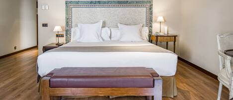 Habitación de hotel con una cama grande, dos mesitas de noche con lámparas, un banco de madera y una silla.