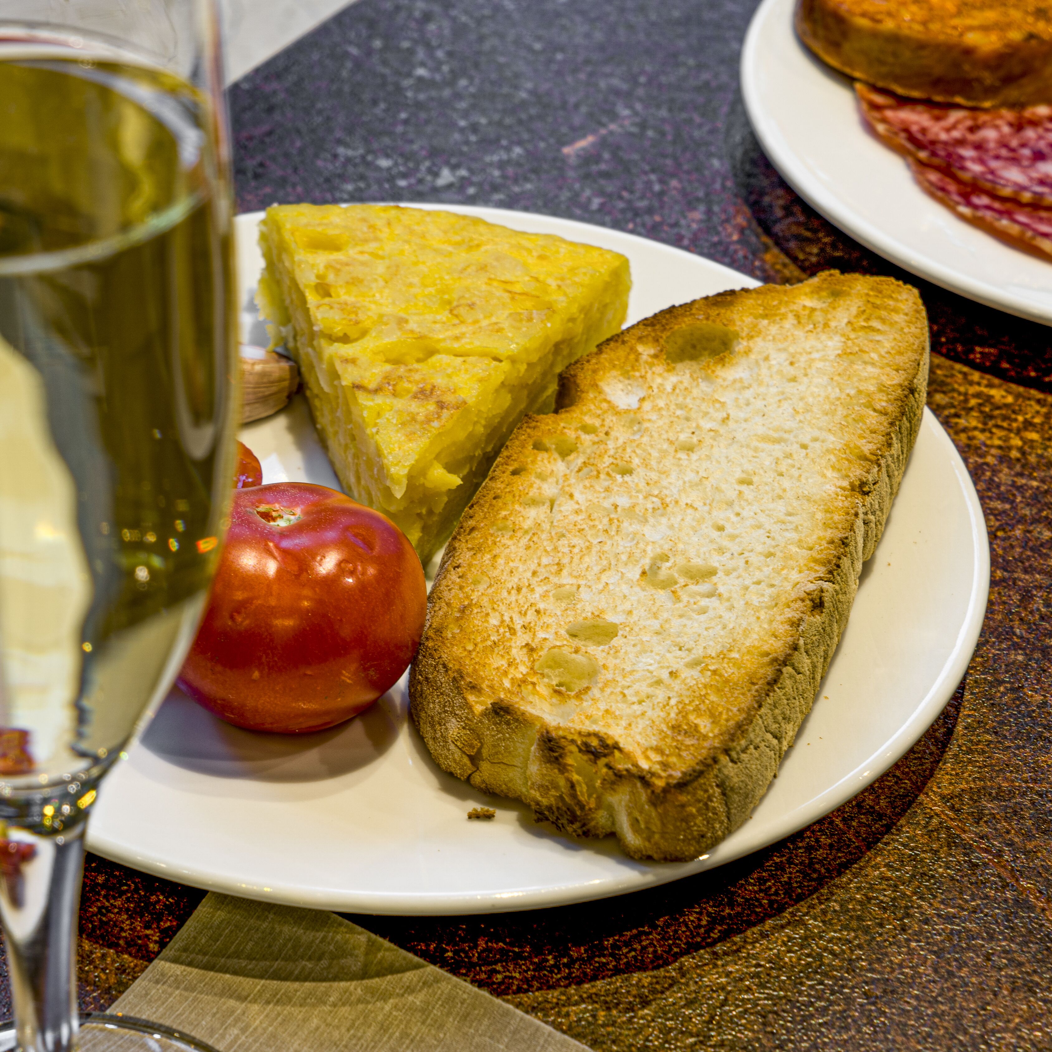 Une assiette avec une tranche de pain, une tomate et un verre de vin blanc, posée sur une table.