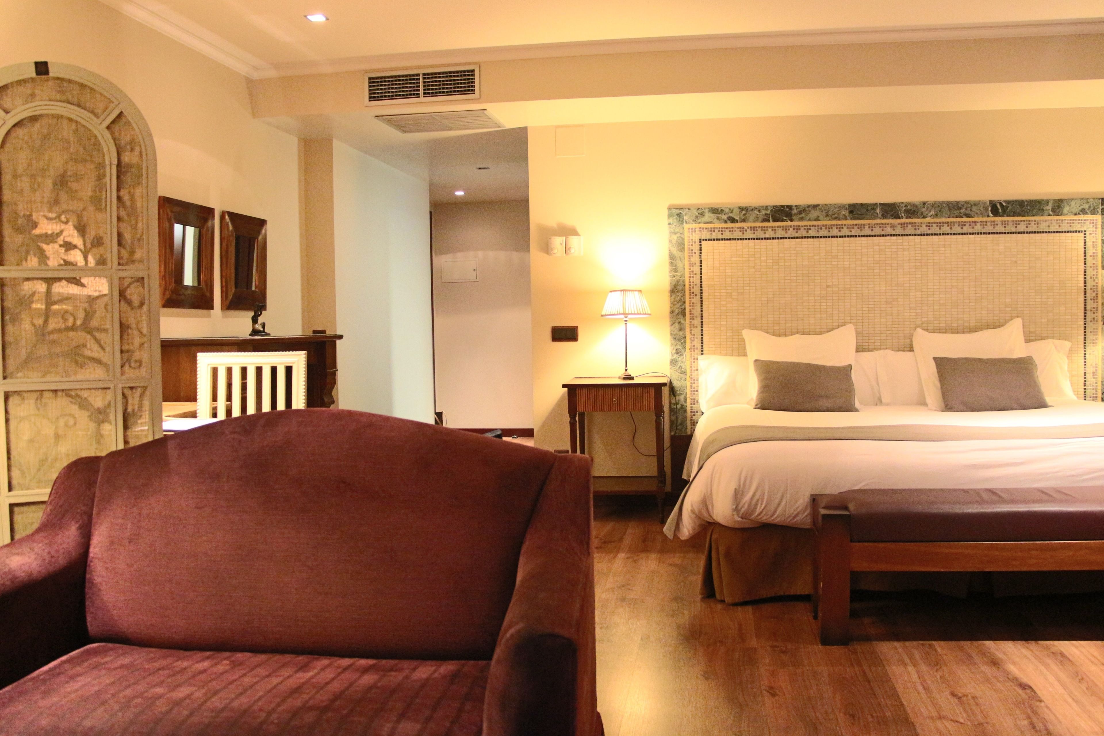 Habitación de hotel con una cama grande, un banco de madera, un escritorio con lámpara y un panel decorativo en la pared.