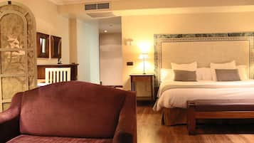 Habitación de hotel con una cama grande, un banco de madera, un escritorio con lámpara y un panel decorativo en la pared.