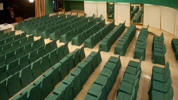 Un salón de conferencias con filas de sillas tapizadas de verde y un escenario con un atril.