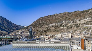 Um edifício moderno com fachada de vidro e painéis solares, cercado por uma paisagem montanhosa e edifícios residenciais.