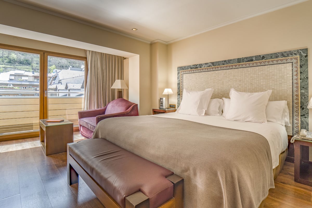 Um quarto espaçoso com uma cama grande, um banco, uma cadeira e vista para o exterior.
