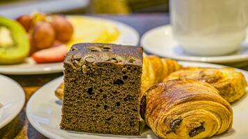A breakfast setting with a loaf of bread, croissants, and a cup of coffee on a table.