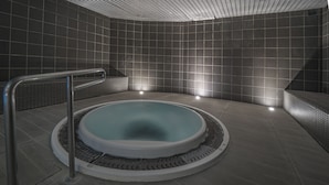 Une salle de spa moderne avec un jacuzzi rond, des garde-corps en métal et des murs carrelés.