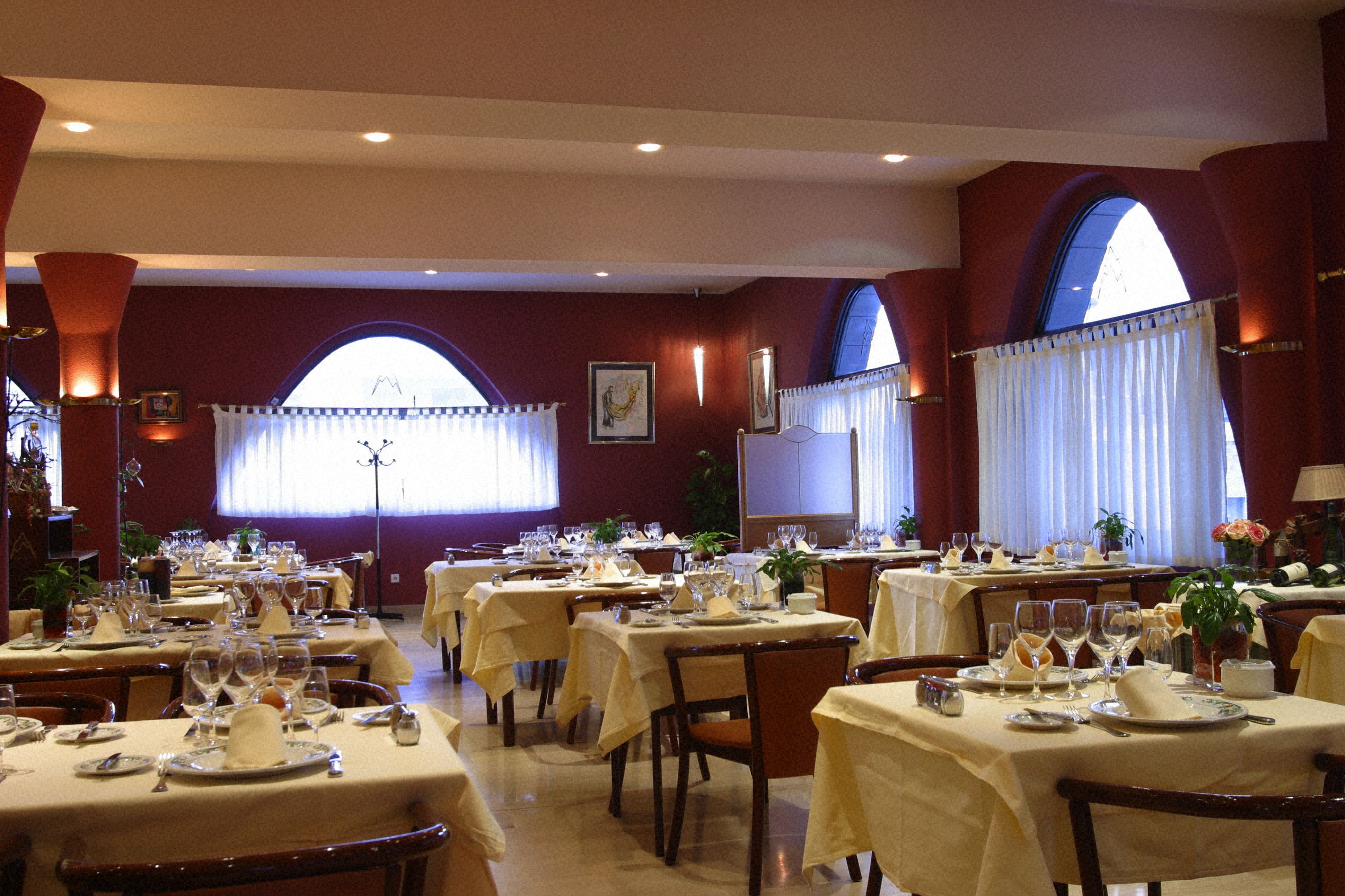 A restaurant with multiple tables set for dining, featuring a classic interior design with arched windows and warm lighting.