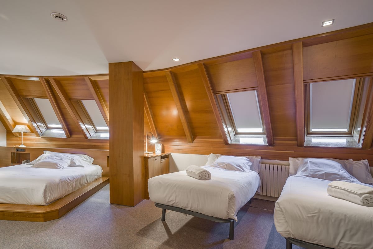 Quarto com duas camas, painel de madeira, claraboias e radiador.