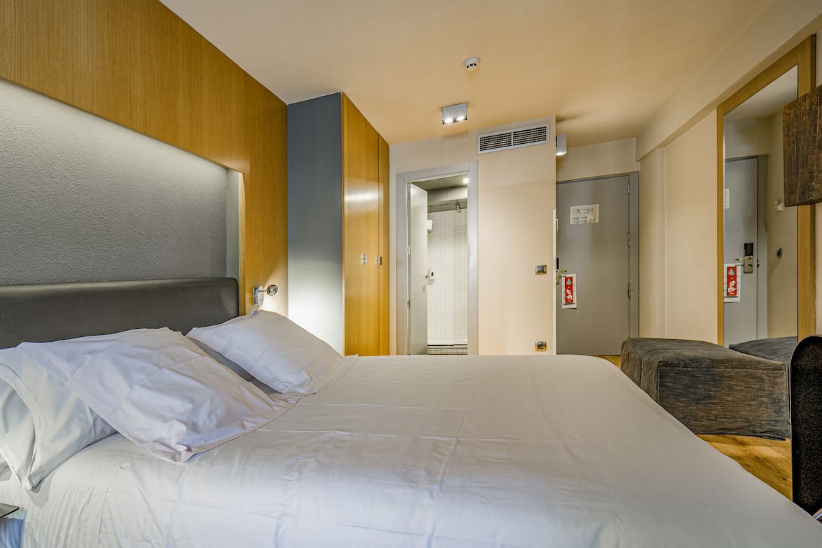 Quarto de hotel com uma cama grande, cabeceira de madeira, mesa de cabeceira e uma cadeira.