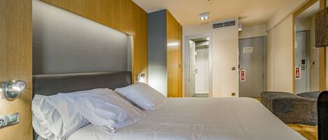 Una habitación de hotel con una cama grande, cabecero de madera, una mesita de noche y una silla.